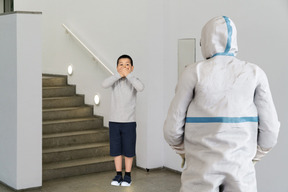 Boy covering mouth in front of person in protective suit