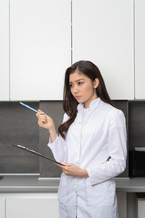 Трехчетвертный вид женщины-врача, указывающей ручкой и держащей планшет