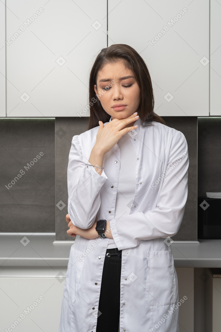 Vista frontale di una dottoressa guardando in basso e toccando il mento