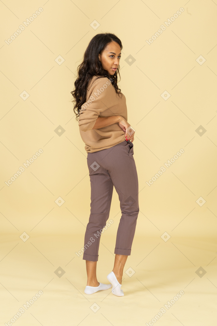 Vista posterior de tres cuartos de una mujer joven de piel oscura enrollando su pulóver
