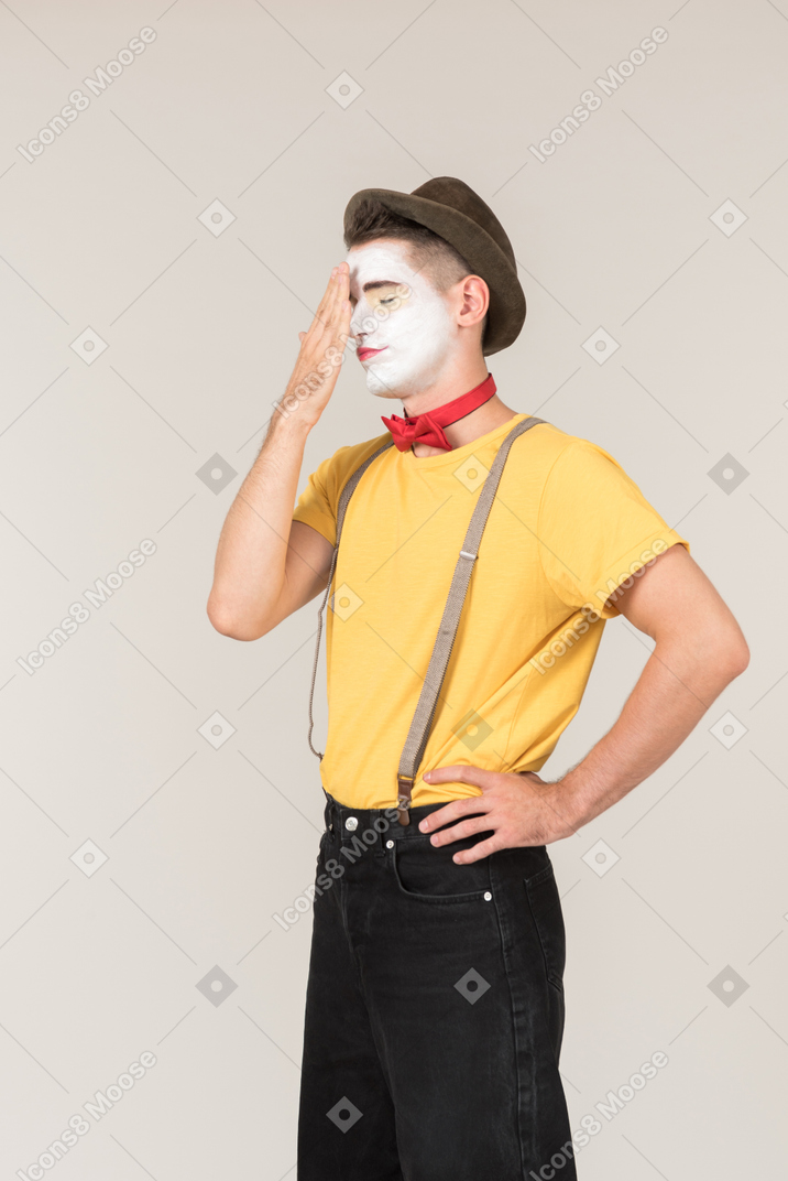 Troubled looking male clown touching his forehead with the hand