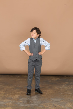 Вид спереди мальчика в сером костюме, позирующего с руками на бедрах