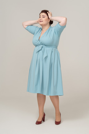 Vista frontal de uma mulher de vestido azul posando com as mãos na cabeça