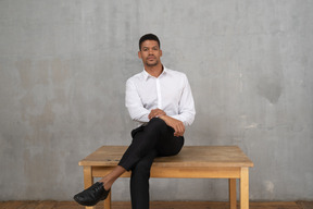 Confident man in formal clothes sitting cross legged on a table