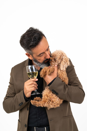 Homem maduro, segurando um copo de vinho e beijando um filhote de cachorro