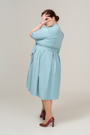 Vista lateral de una mujer en vestido azul mirando a través de los dedos