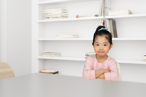 A little girl sitting at a table in front of a book shelf