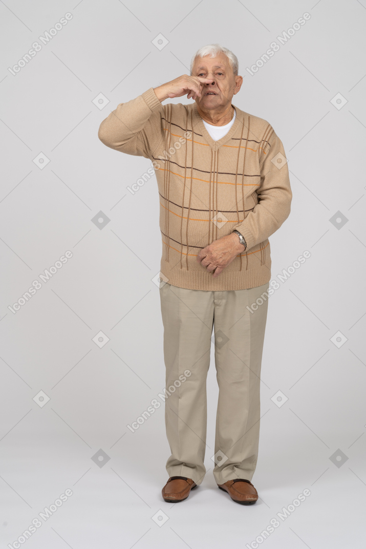 Front view of an old man in casual clothes touching nose