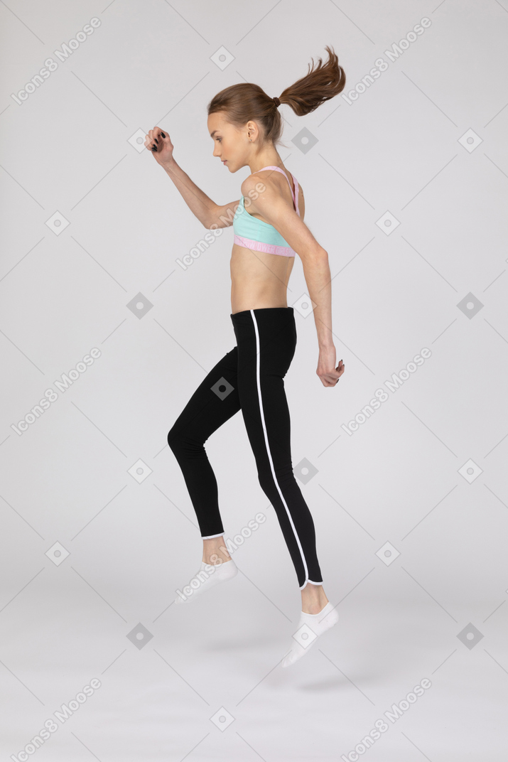 Vista lateral de una jovencita en ropa deportiva levantando la mano y saltando