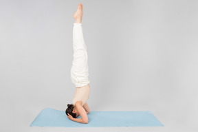 Jeune femme indienne debout sur la tête sur un tapis de yoga