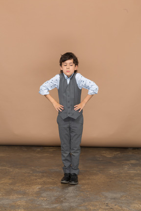 Vista frontal de un chico lindo con traje gris posando con las manos en las caderas