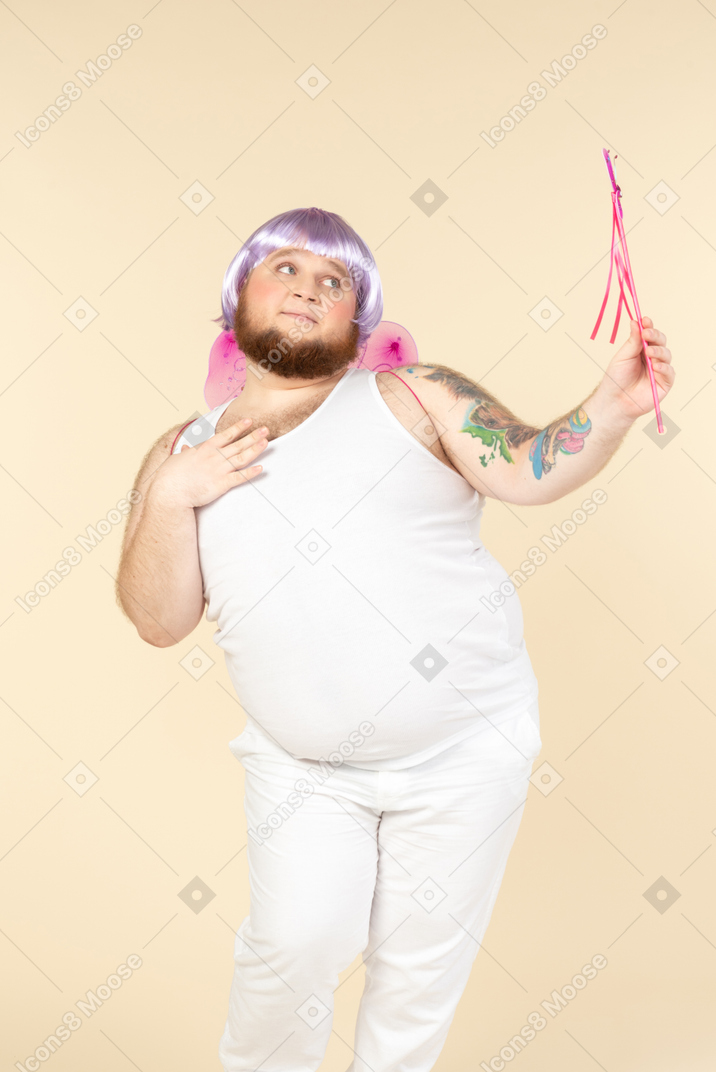 Dreamy looking young overweight man dressed as a fairy holding fairy wand