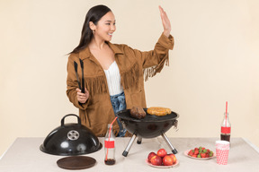 Joven mujer asiática preparando barbacoa y saludando con la mano