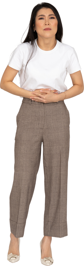 Vista frontale di una giovane donna in calzoni e maglietta che tocca il suo stomaco
