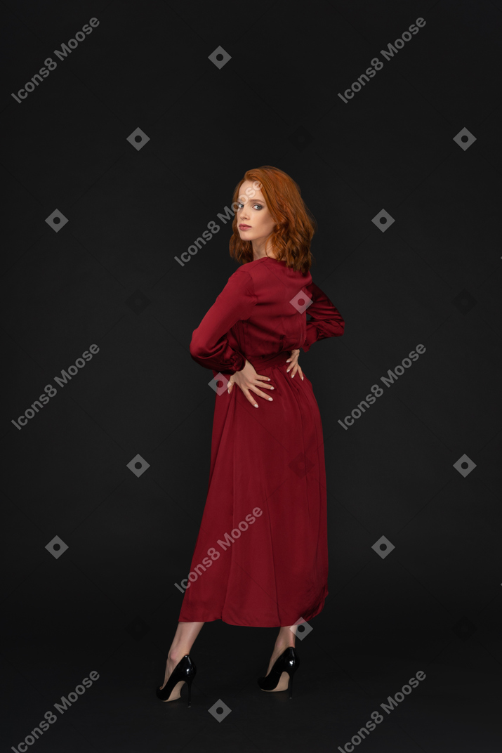 A three-quarter back side view of a beautiful sexy woman dressed in red and looking to the camera