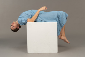 Side view of young woman lying on cube