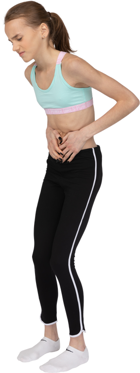 Vista de tres cuartos de una adolescente en ropa deportiva tocando el estómago e inclinándose