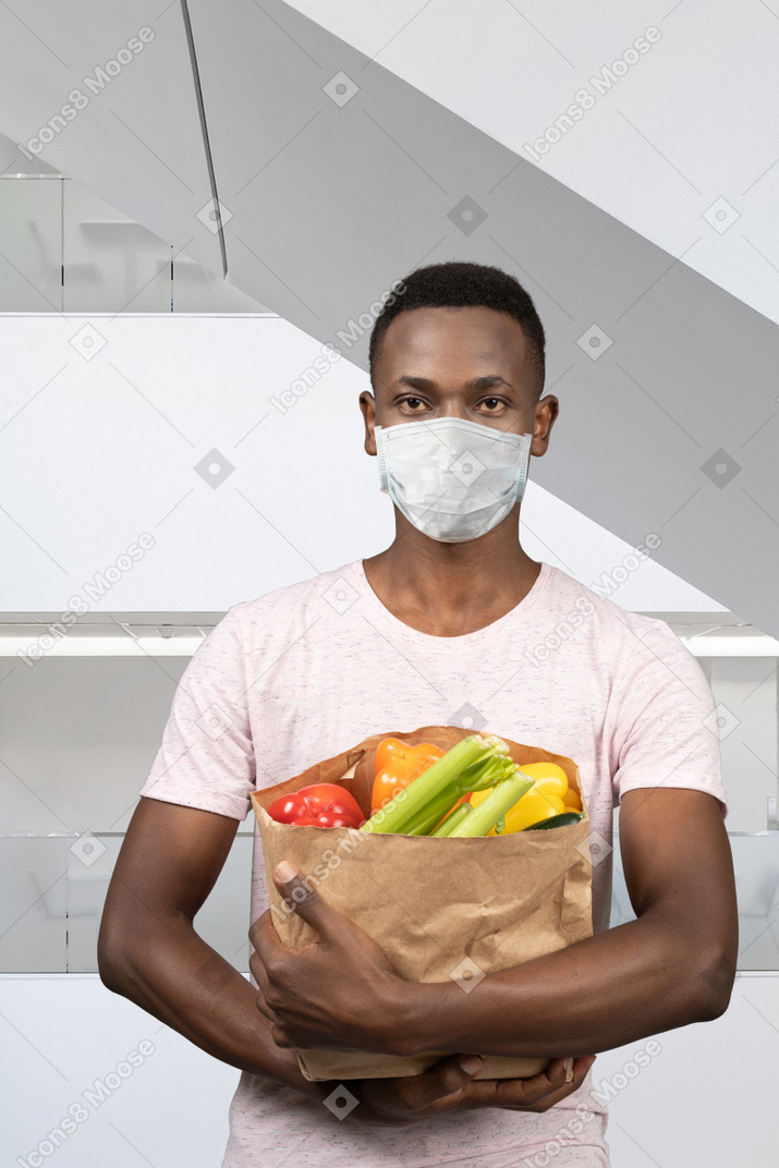 A man wearing a face mask holding a bag of vegetables