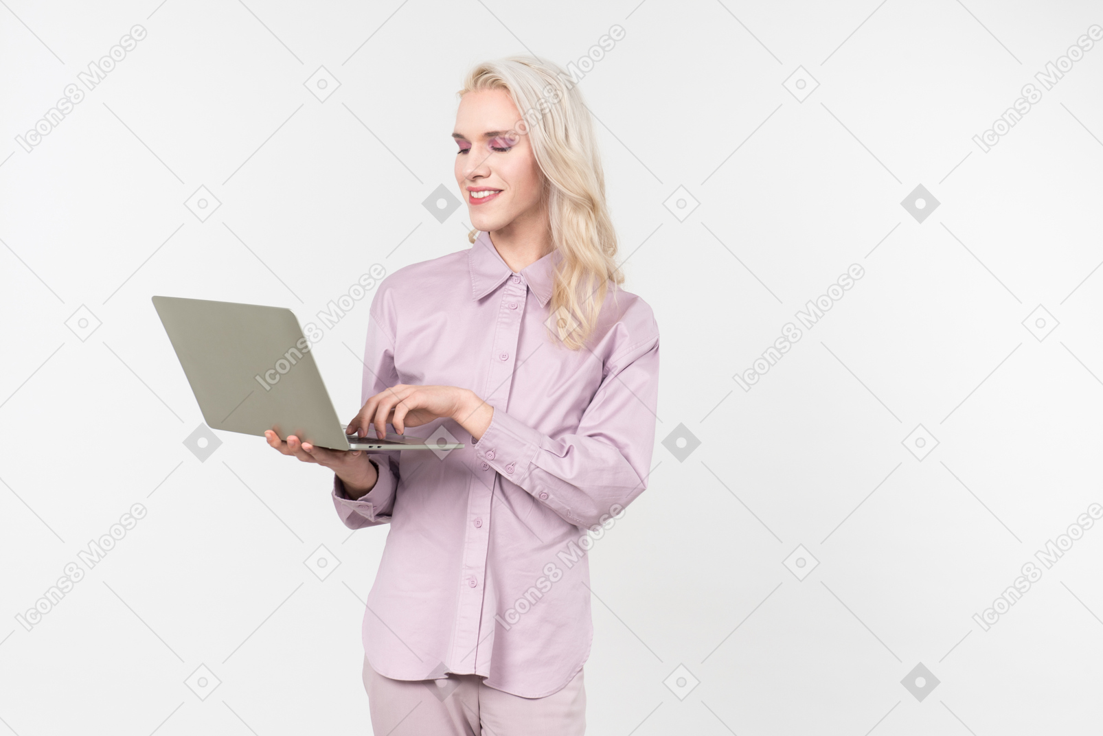 Young blond-haired person in pastel clothes and with a laptop in their hand, communicating with someone through the internet, standing against a plain white background