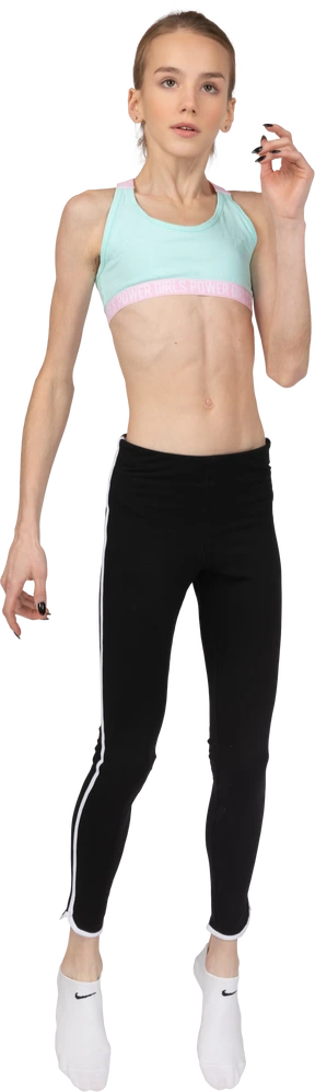 Three-quarter view of a teen girl in sportswear raising hand while squatting