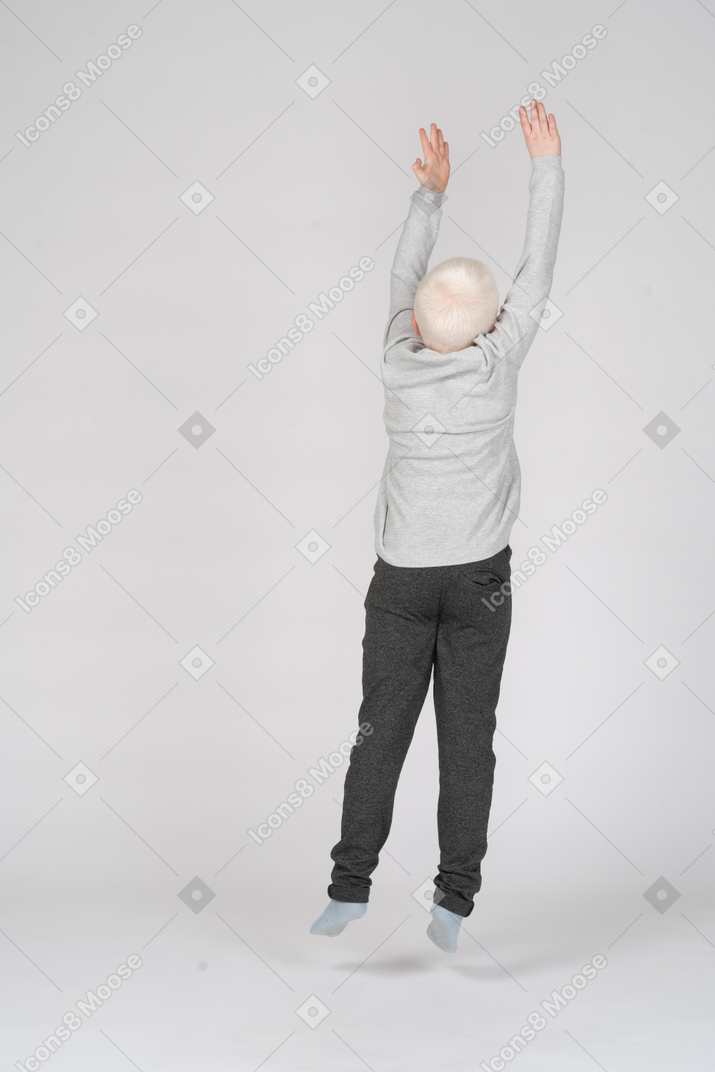 Vista traseira de um menino pulando com as mãos no ar