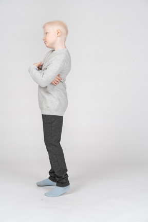 Vista lateral de um garoto travesso balançando a cabeça enquanto cruza as mãos