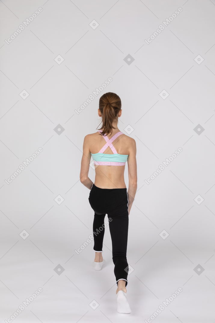 Vista traseira de uma adolescente em uma roupa esportiva dando uma estocada