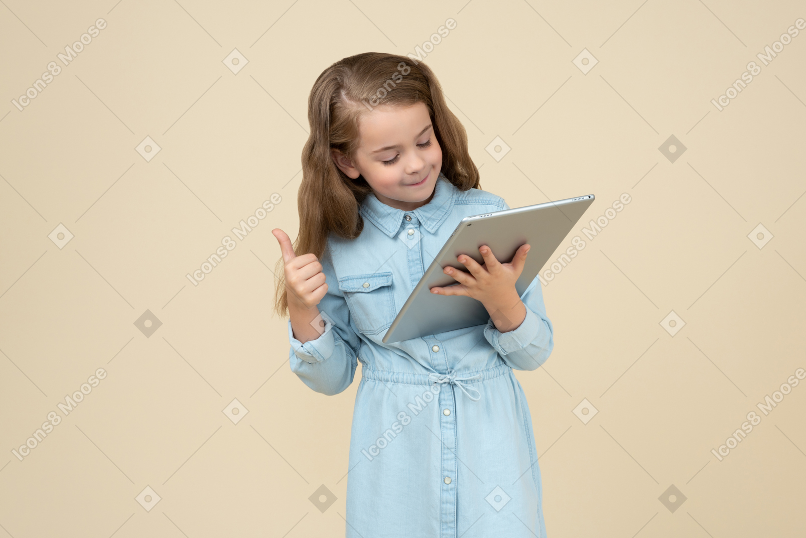 Cute little girl holding a tablet and showing thumbs up