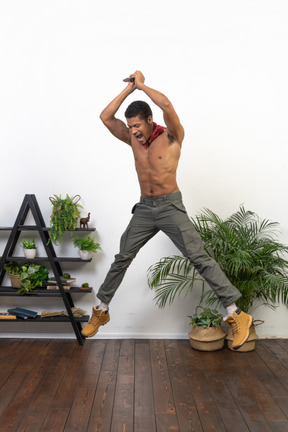 Muscular man with a knife in raised hands jumping up