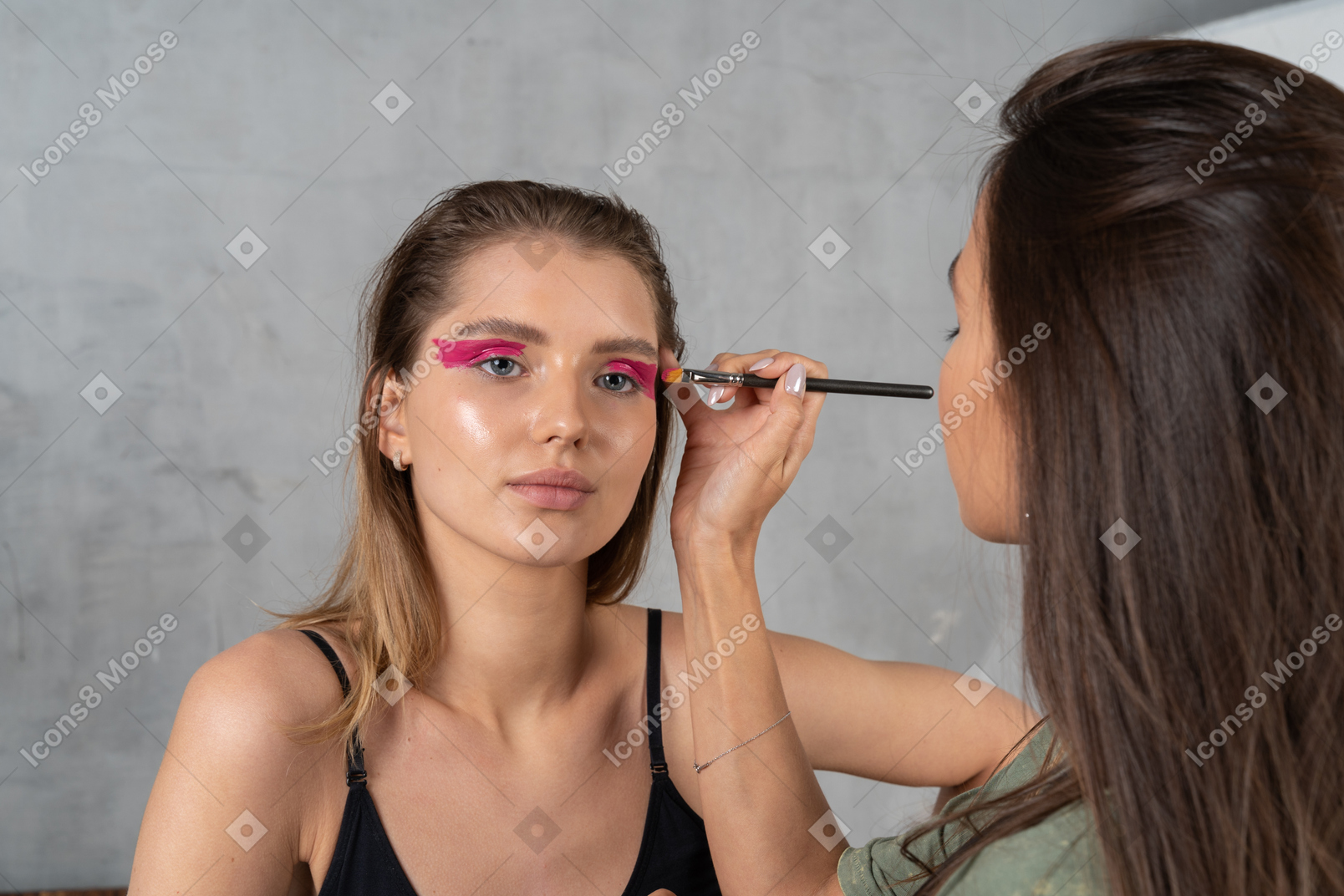 Vue de face d'une jeune femme avec un maquillage des yeux rose vif et sa maquilleuse