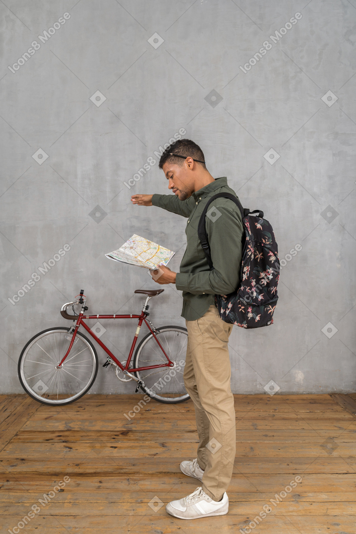 Seitenansicht eines mannes mit rucksack, der auf eine karte schaut und zur seite zeigt