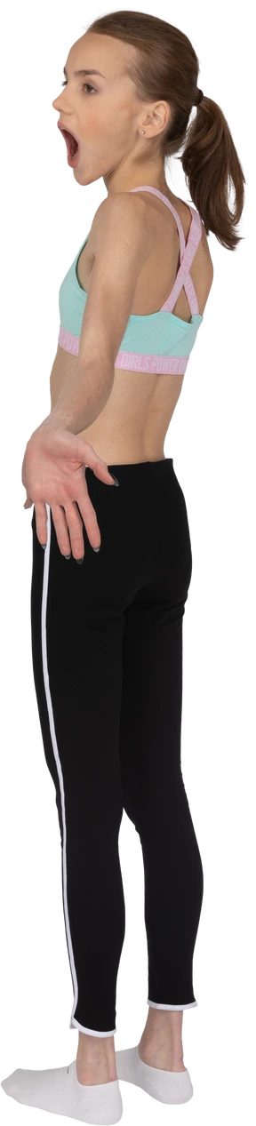 Three-quarter back view of a surprised teen girl in sportswear outspreading hands and opening her mouth
