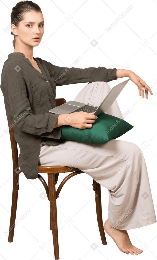 一位穿着家居服的年轻女子坐在椅子上，拿着笔记本电脑的侧视图