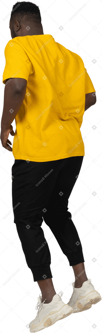 黄色のtシャツを着てジャンプする若い浅黒い肌の男の4分の3の背面図