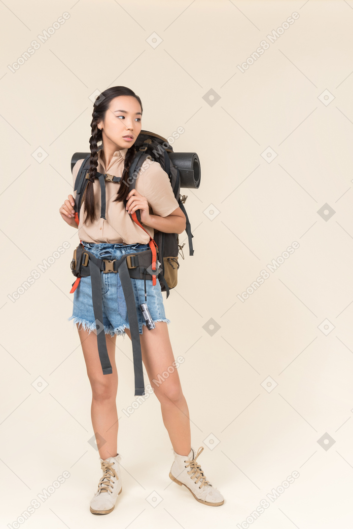 Joven mujer asiática excursionista de pie con mochila y mirando a un lado