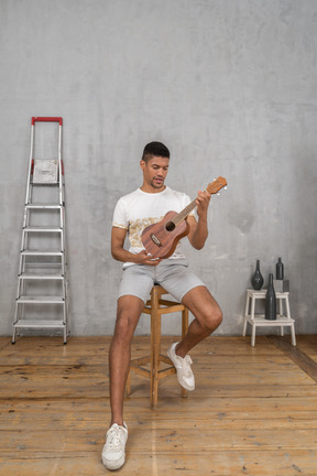 Vista frontal de um homem em um banquinho examinando um ukulele