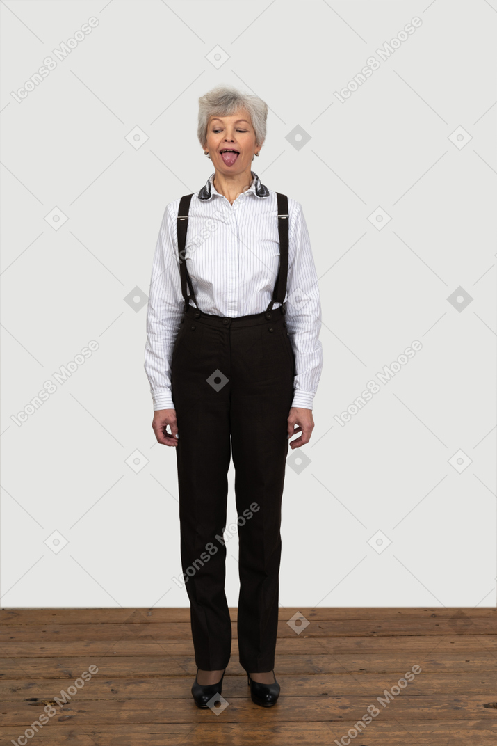 Front view of an old female in office clothes standing still indoors with her eyes closed showing a tongue