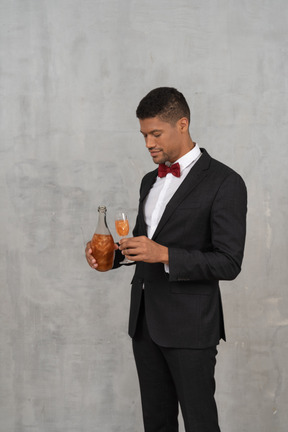 Hombre sosteniendo una botella y una copa de champán y mirando hacia abajo