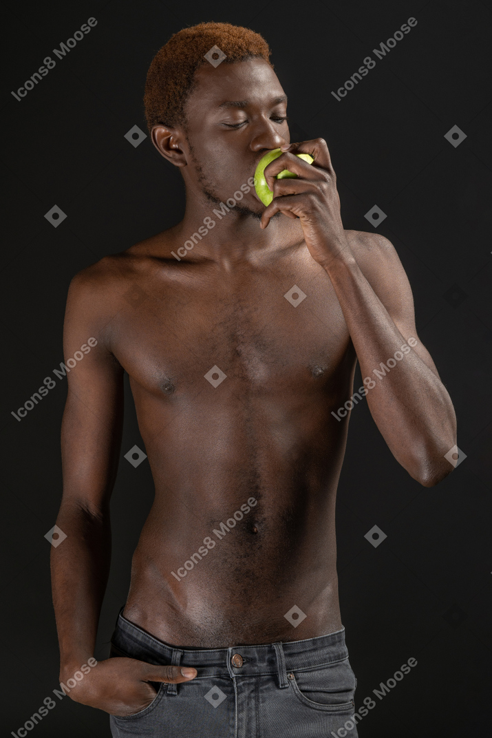 Close-up an african young man biting an apple with his eyes closed