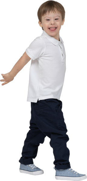 Vista lateral de um menino andando e mostrando a língua de brincadeira