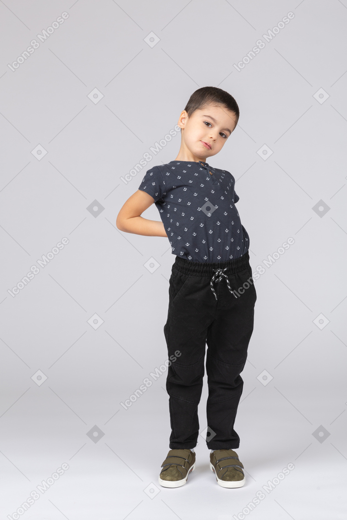 一个穿着休闲服的可爱男孩的前视图，双手背在背上，看着相机
