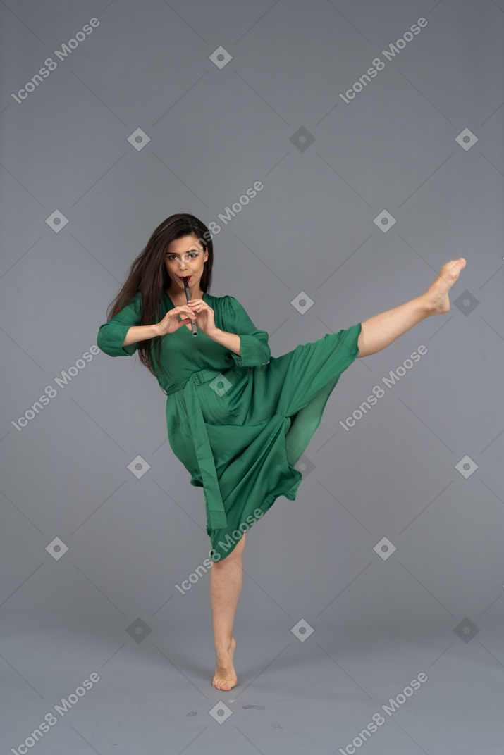 Vista frontale di una giovane donna che balla in abito verde, suonare il flauto