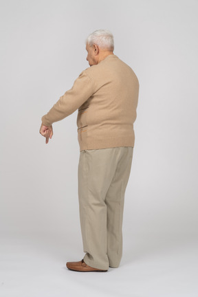 Vista lateral de un anciano con ropa informal apuntando hacia abajo con un dedo