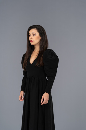 Three-quarter view of a young lady in a black dress standing still