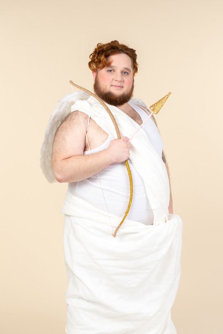 Cunning looking young man dressed as a cupid holding bow and arrow