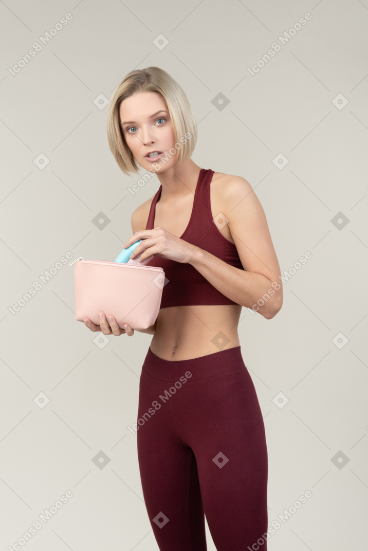 Pensive young woman in sportswear holding cosmetic bag