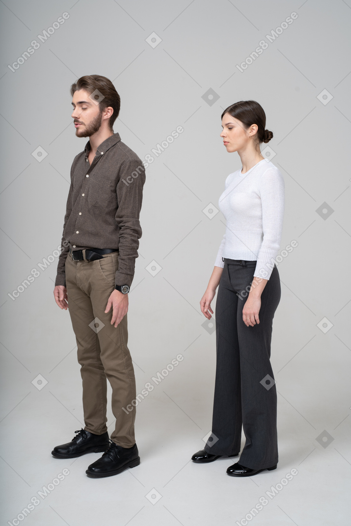 Трехчетвертный вид молодой пары в офисной одежде, стоящей с закрытыми глазами