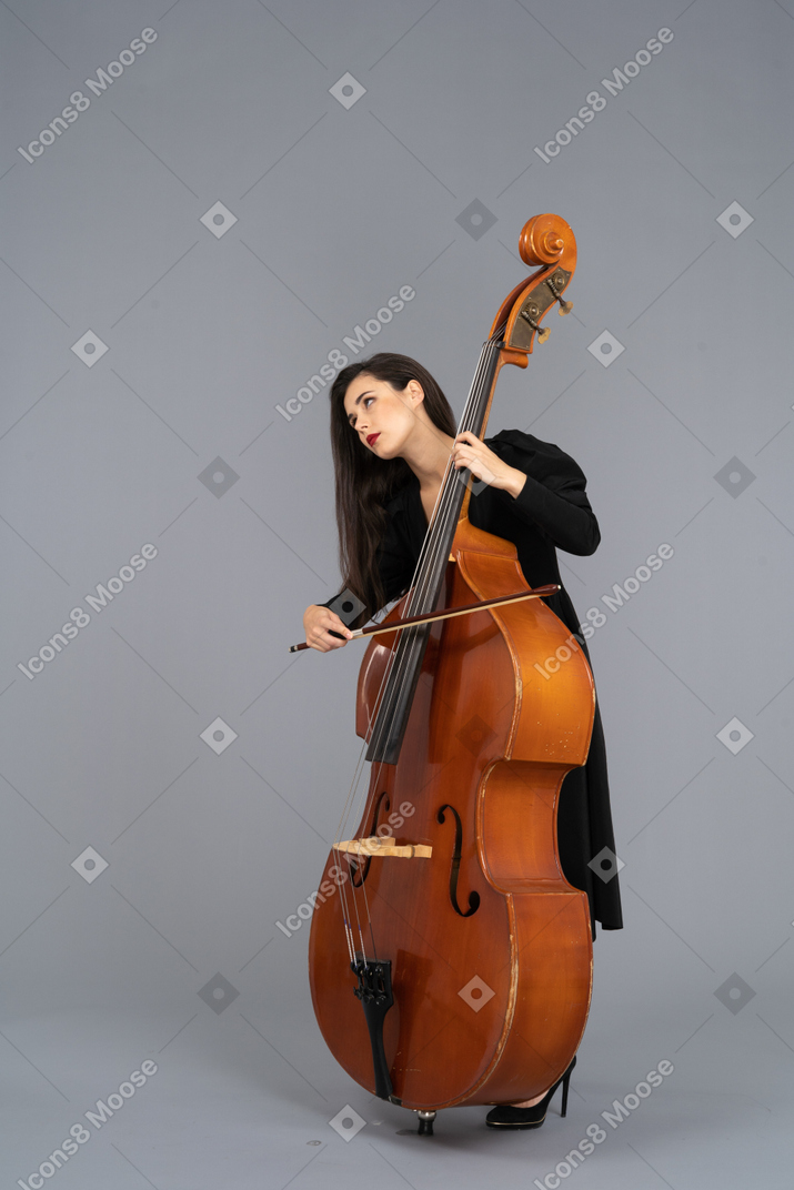 Dreiviertelansicht einer jungen frau im schwarzen kleid, die den kontrabass mit einer schleife spielt