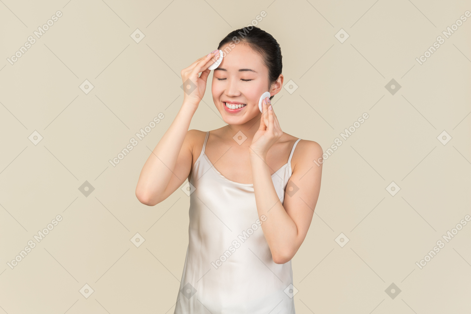 Улыбающаяся молодая азиатская женщина с закрытыми глазами чистит лицо ватными подушками