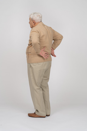 Vista lateral de um velho em roupas casuais, sofrendo de dor nas costas